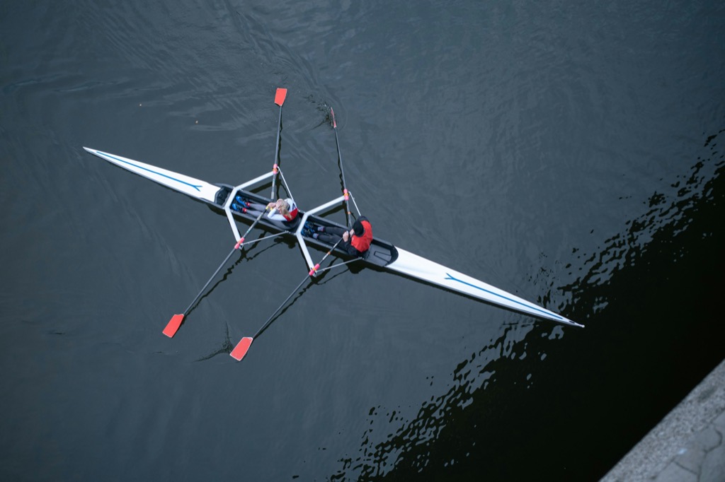 A double scull seen from above on dark water, the oars in the drive