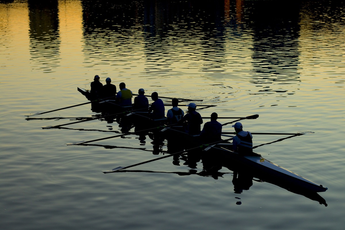 An eight in silhouette on mirror-flat water at dusk, the oars above the water